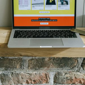 A laptop on a wooden shelf showing a colorful online shopping webpage.