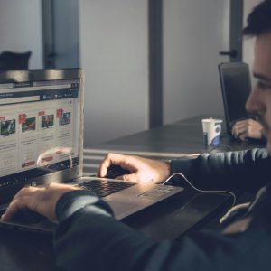 Adult man using laptop to browse an online marketplace in a modern office.